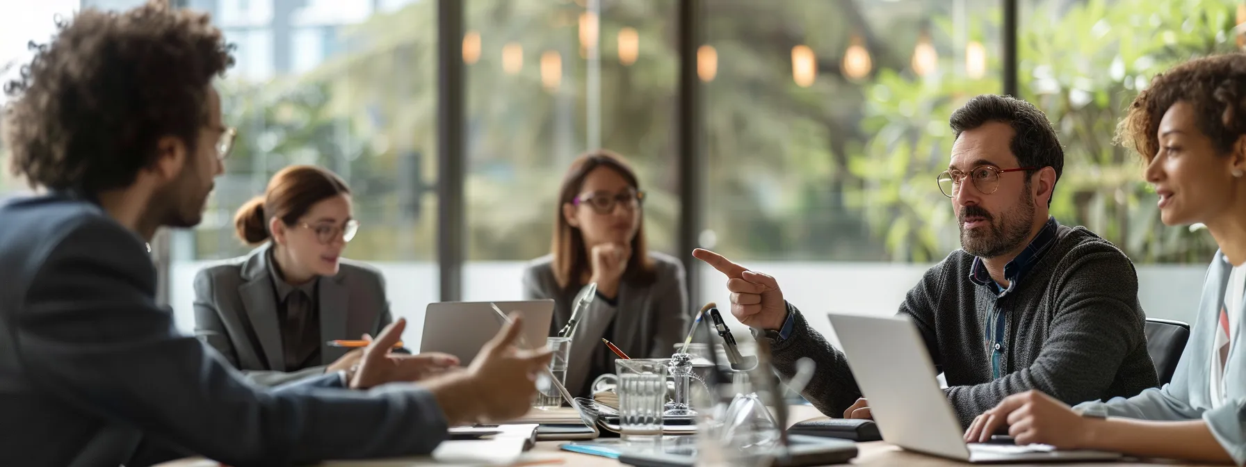 a group of professionals engaged in a lively discussion around a table with laptops open, pointing at a visual representation of online communication courses.